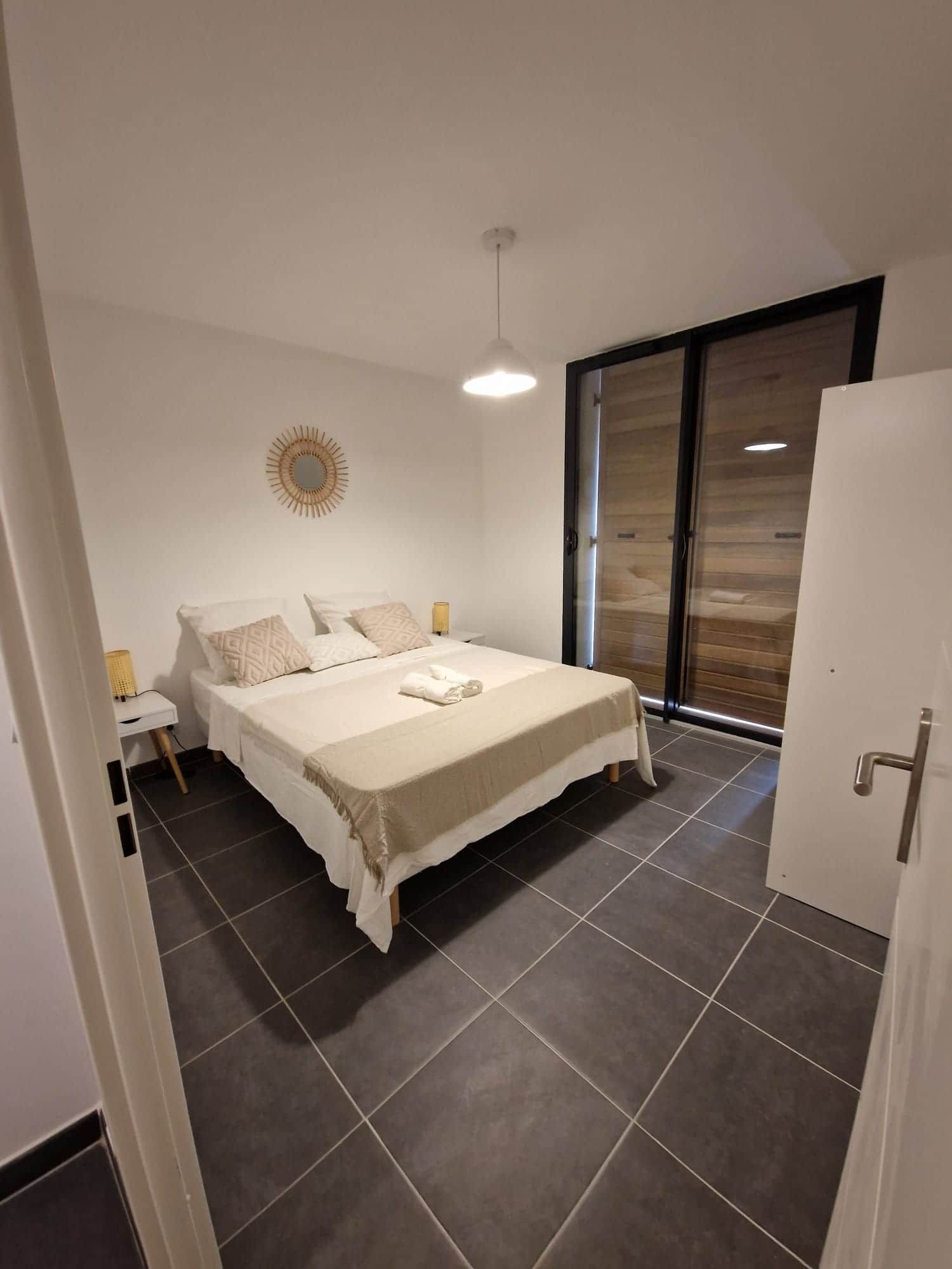 Ein Schlafzimmer mit einem Bett, einem Nachttisch, einer Wanduhr und einer Glasschiebetür, die auf einen Balkon führt.