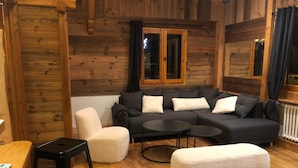 A cozy log cabin interior with a sectional sofa, a small round table, a cushioned stool, and a wooden floor. - Tourist chalet (La Salle-les-Alpes)