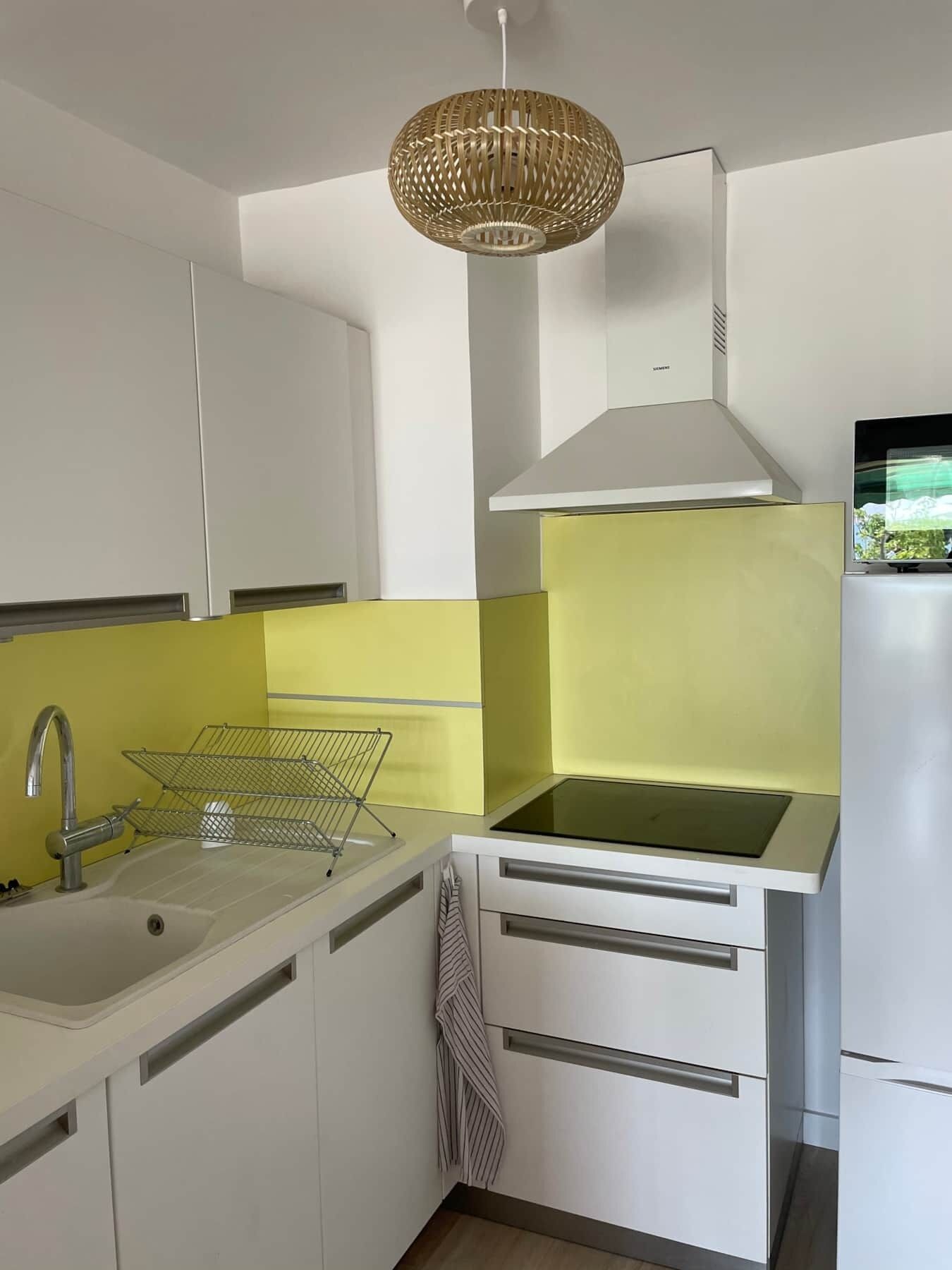 Une cuisine compacte avec des meubles blancs, un crédence jaune, un évier en acier inoxydable et une cuisinière moderne.