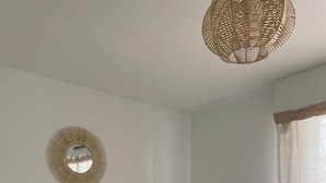 A minimalist bedroom with a bed, a round mirror, and a woven light fixture.