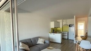A modern living room with a grey sofa, a white coffee table, and a dining area with a white table and chairs.
