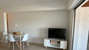 A modern living room with a dining area, a flat-screen TV, and a sliding glass door leading to a balcony.