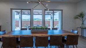 A spacious dining area with a large wooden table and six chairs, large windows offering a view of the outdoors, and a modern ceiling light fixture. - Arcadia 55 | Pool Table * PRIVATE Hot Tub * BBQ (Santa Clara)