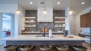 A modern kitchen with a large island, pendant lights, wooden stools, and built-in shelves. - Arcadia 55 | Pool Table * PRIVATE Hot Tub * BBQ (Santa Clara)