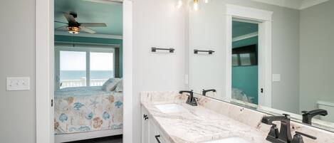 A bathroom with a double sink, a ceiling fan, and a large mirror.