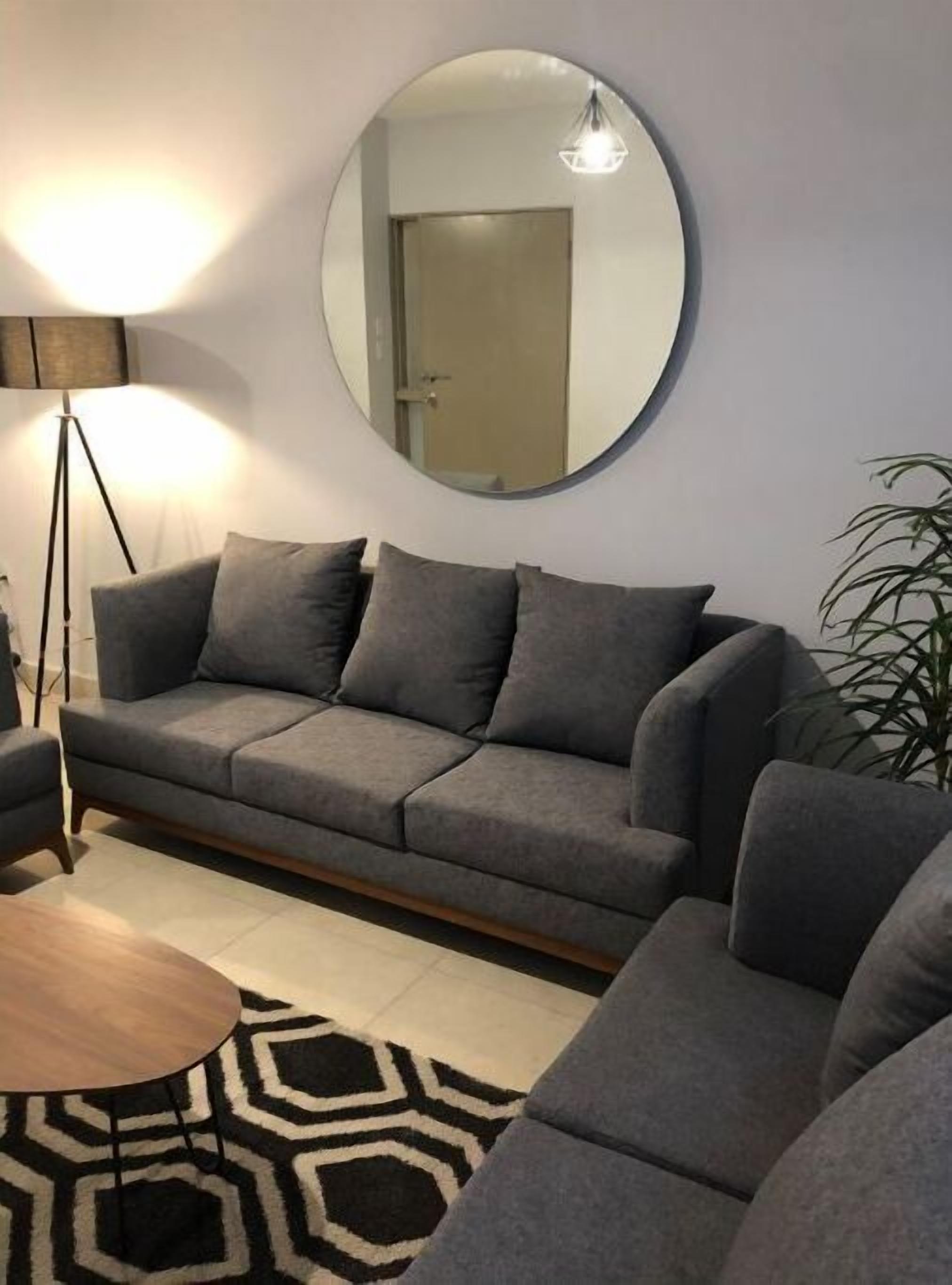 A modern living room with a grey sofa, a round mirror, a floor lamp, and a patterned rug.