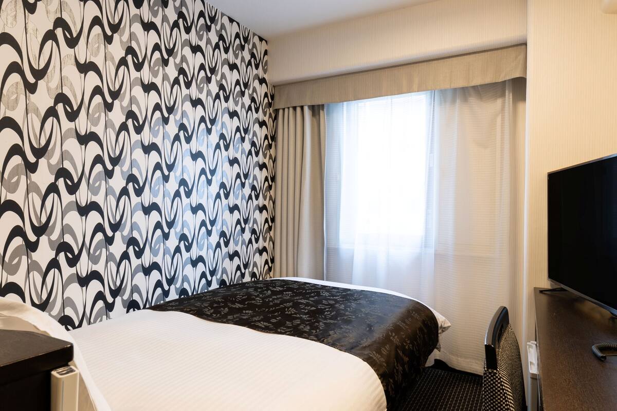 A hotel room with a large bed, a television, and a window with curtains.