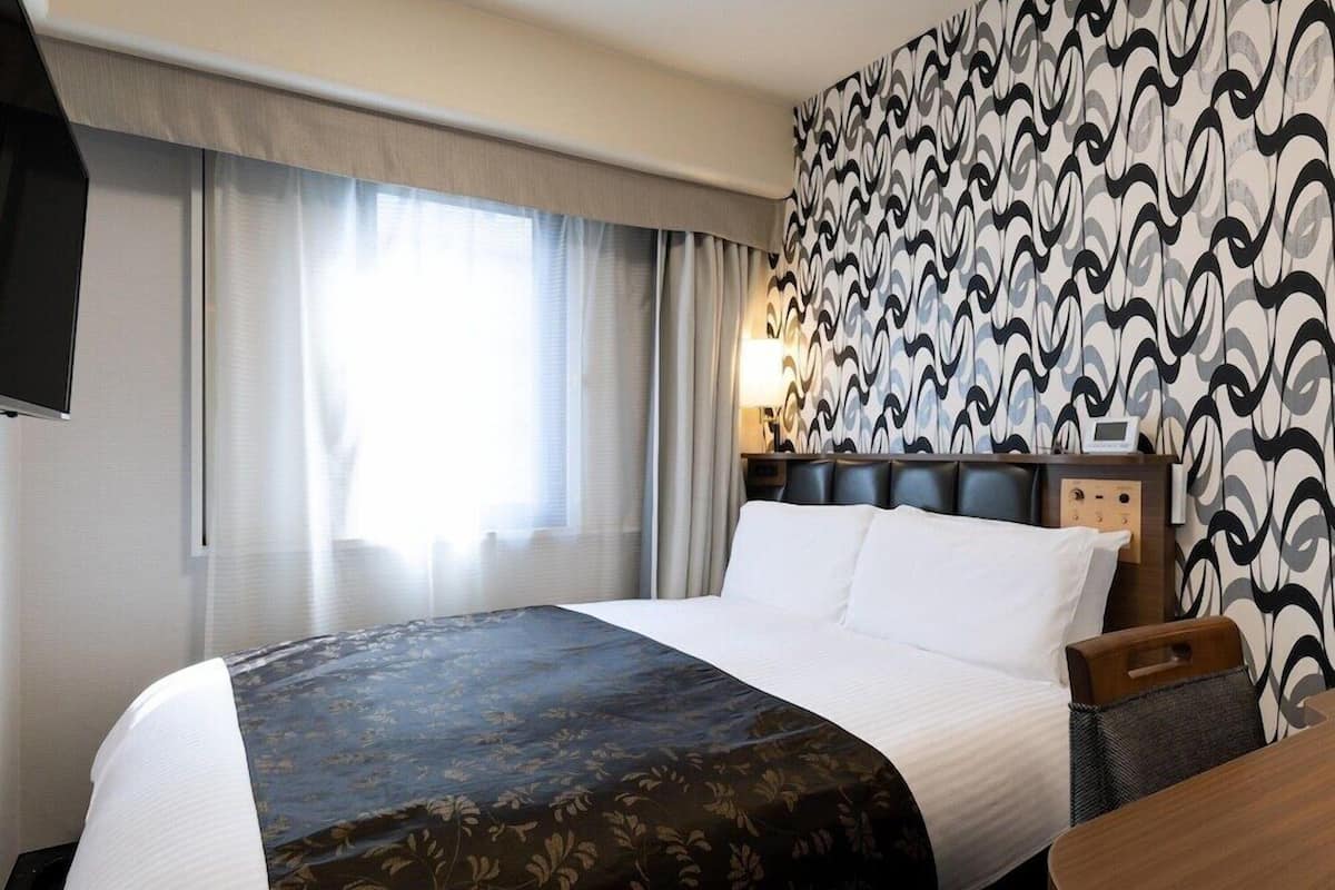 Una habitación de hotel con cama, mesita de noche, lámpara y pared con diseño.