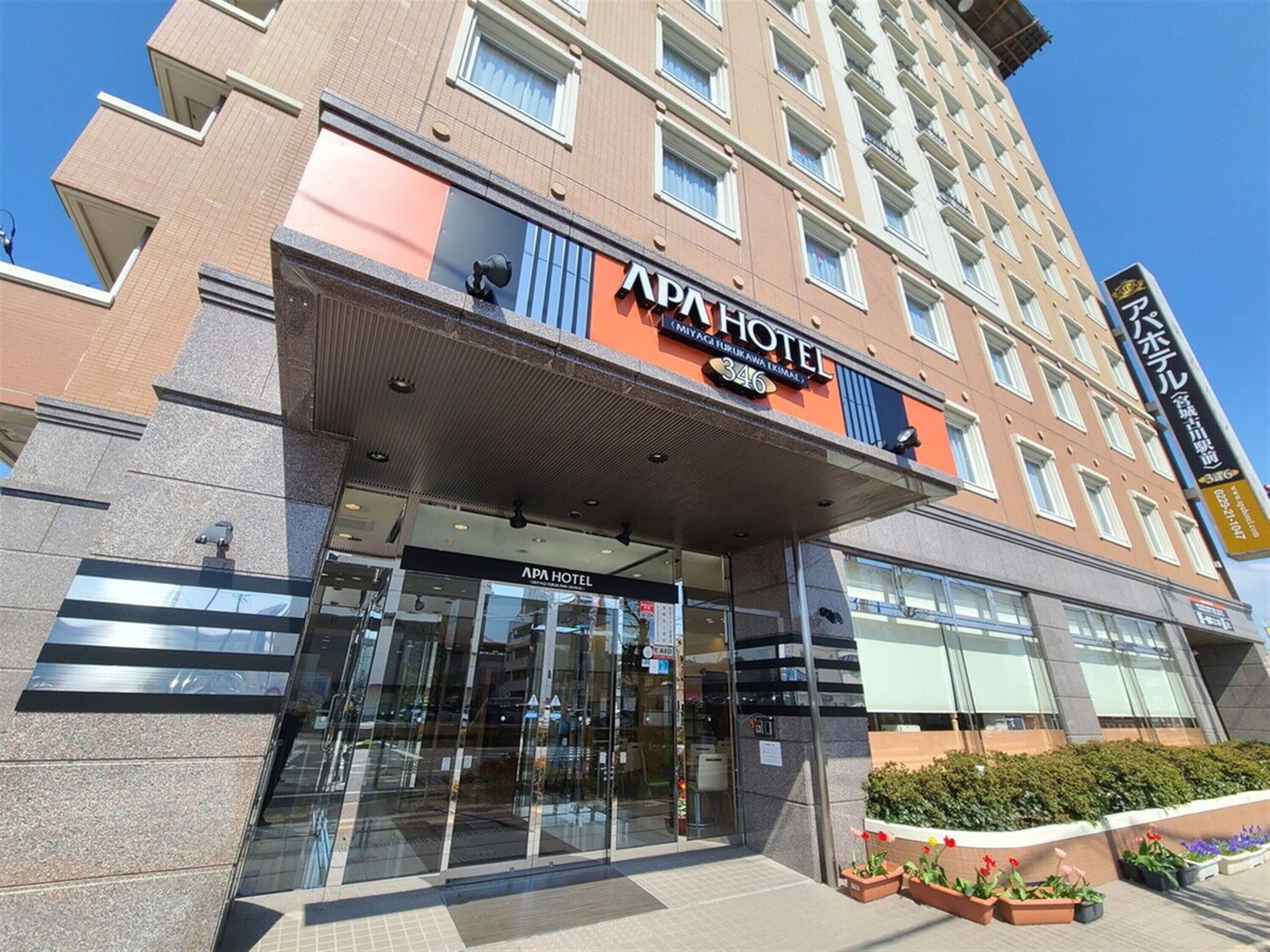 The APA HOTEL entrance with a modern design, including a glass facade and a covered entrance area.