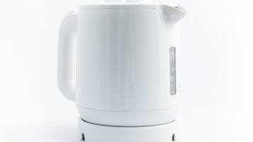 Una tetera eléctrica blanca con asa y pico, sobre una base blanca.