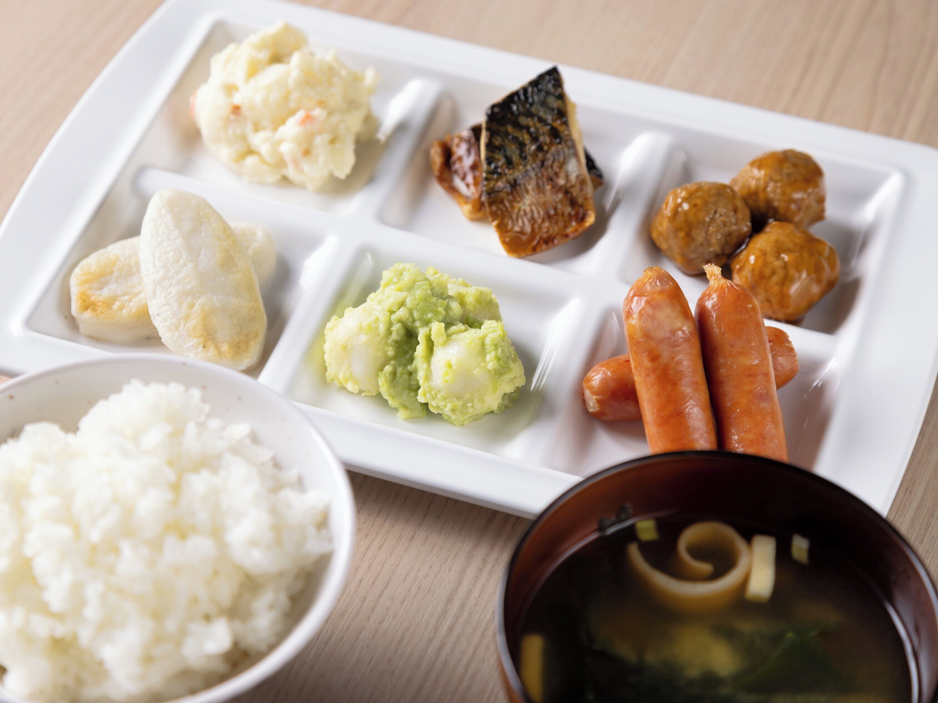 En vit, rektangulär tallrik med olika japanska rätter, inklusive ris, misosoppa och grillad fisk.