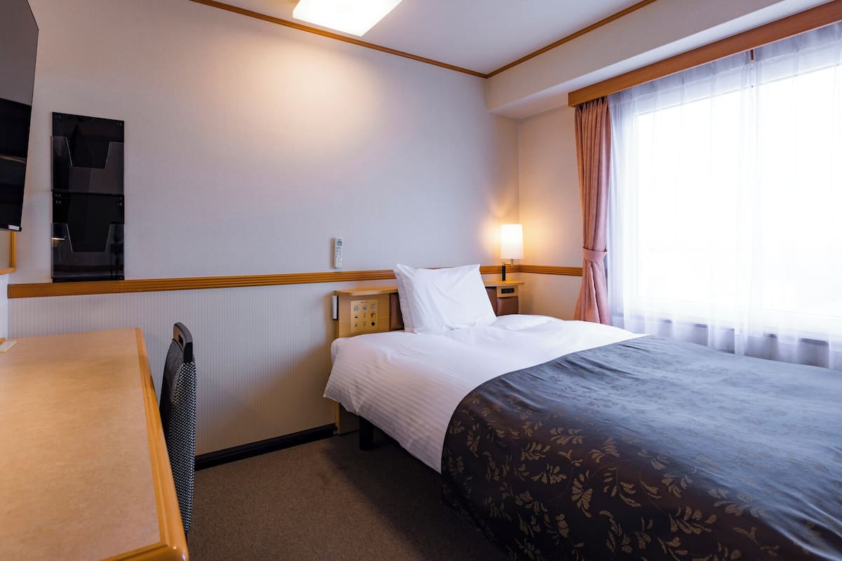 A hotel room with a bed, bedside table, lamp, and a flat-screen TV mounted on the wall.