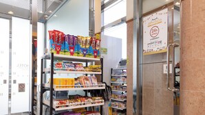 Un présentoir de collations dans un magasin, avec divers produits emballés et un panneau indiquant que le magasin est ouvert 24 heures sur 24.