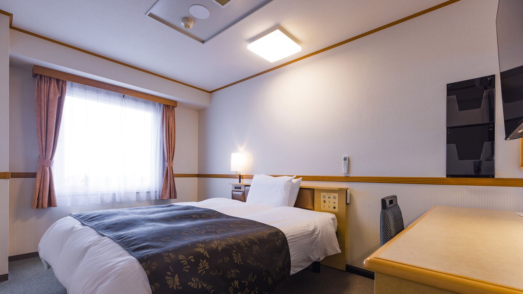 Een hotelkamer met een bed, nachtkastje, lamp en een klein bureau.