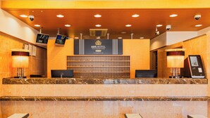 Un comptoir d’accueil d’hôtel doté d’un écran numérique, un espace d’attente avec des sièges et un tapis à motifs.