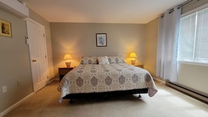 Een slaapkamer met een groot bed, twee nachtkastjes met lampen, een deur en een raam met zonwering.