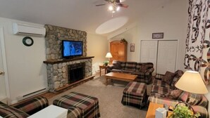 A living room with a stone fireplace, plaid furniture, a television, and a ceiling fan.