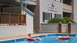 Uma área de piscina com duas pessoas em boias, uma placa da Nordic Inn e um edifício com varanda.