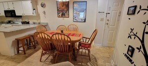 Comedor con mesa redonda y sillas de madera, cocina con alacenas blancas y una pared con un adhesivo de árbol.