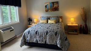 Quarto com uma cama grande, duas mesas de cabeceira com luminárias, um quadro na parede e uma janela com cortinas.