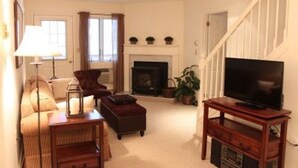 Una sala de estar con sofá, sillón, mesa de centro, chimenea, televisor y escalera.