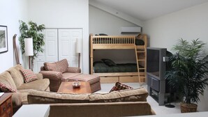 Un espacio habitable compacto con una cama litera, un conjunto de sofás, un televisor y una planta en maceta.