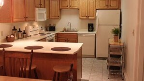 Una cocina compacta con armarios de madera, una isla central con taburetes, un microondas, una cafetera y un refrigerador.
