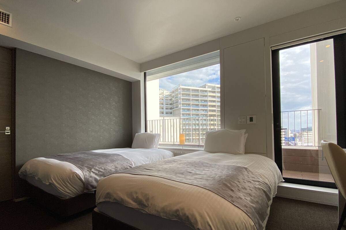 Een moderne hotelkamer met twee bedden, een groot raam met uitzicht over de stad en een balkon.