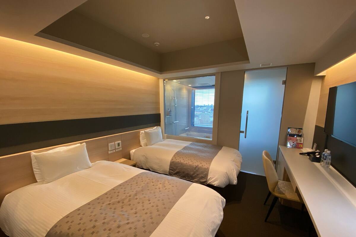 Een hotelkamer met twee bedden, een bureau en een raam met uitzicht op de stad.