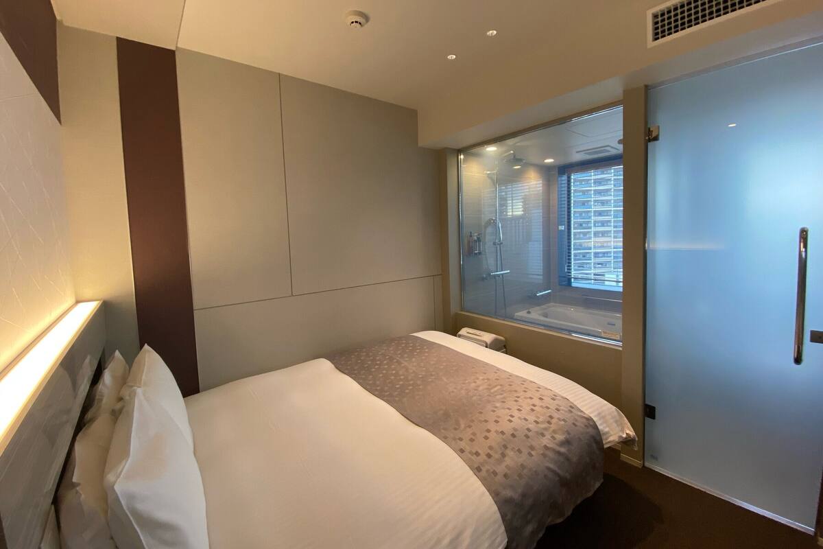 Een moderne hotelkamer met een bed, een raam met uitzicht over de stad, een douche en een deur.