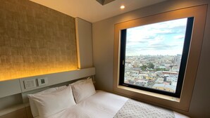A hotel room with a large bed, a headboard with built-in lighting, a window with a city view, and a control panel for room amenities. - APA Hotel Keikyukamata Ekimae (Tokyo)