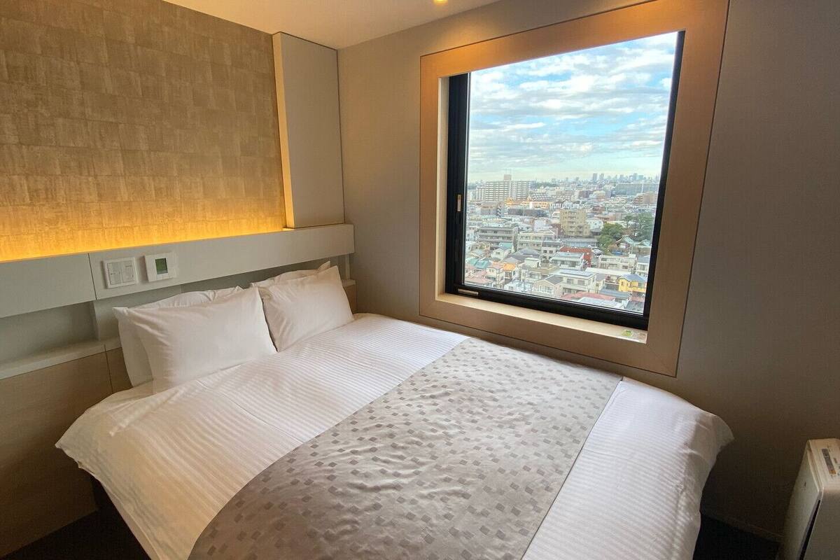 Een hotelkamer met een bed, een raam met uitzicht op de stad, een wandlamp en een radiator.