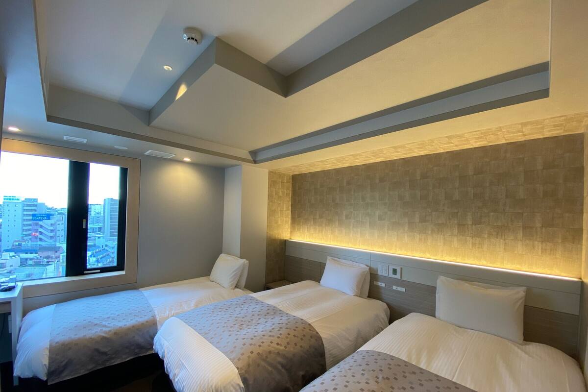 Een hotelkamer met twee bedden, een groot raam met uitzicht op de stad, en een modern design met een patroon op de wand en het plafond.