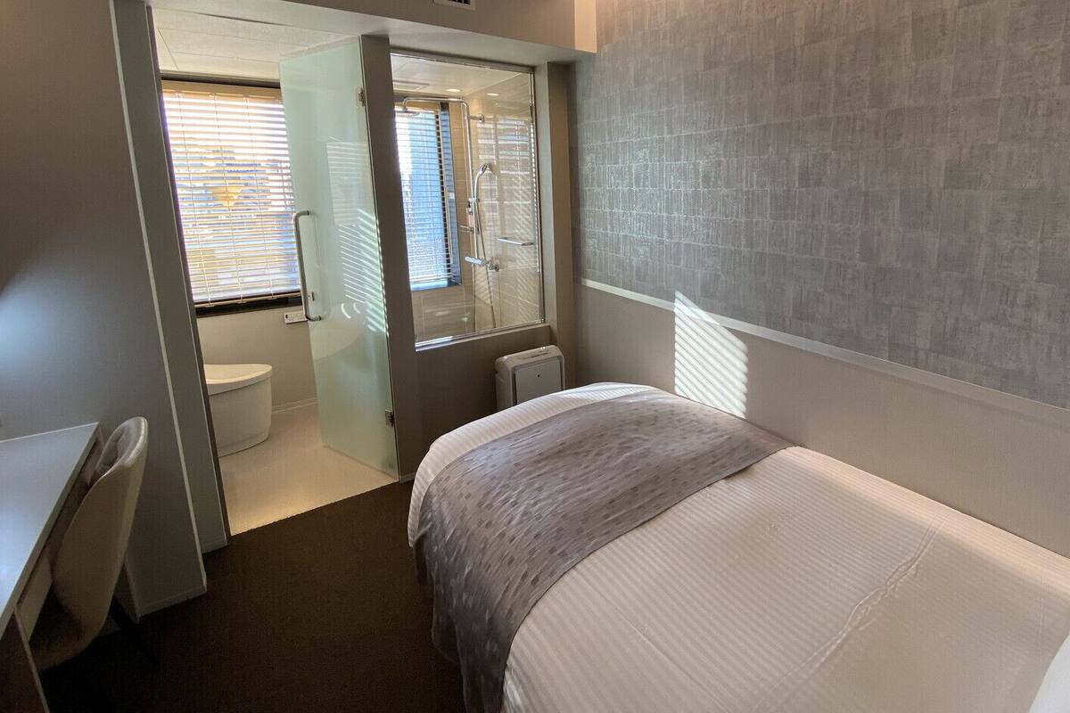 Een hotelkamer met een bed, een bureau, een stoel, een raam met jaloezieën en een douche.