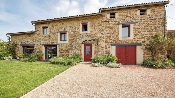 A two-story stone building with a red door and windows, surrounded by a gravel driveway and greenery. - Family suite on 2 levels in a peaceful hamlet. Ideal for families (LE VERNET LA VARENNE)