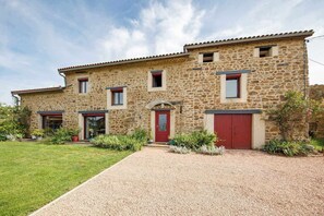 A two-story stone building with a red door and windows, surrounded by a gravel driveway and greenery. - Two-level family suite in a quiet hamlet. Ideal for families (LE VERNET LA VARENNE)