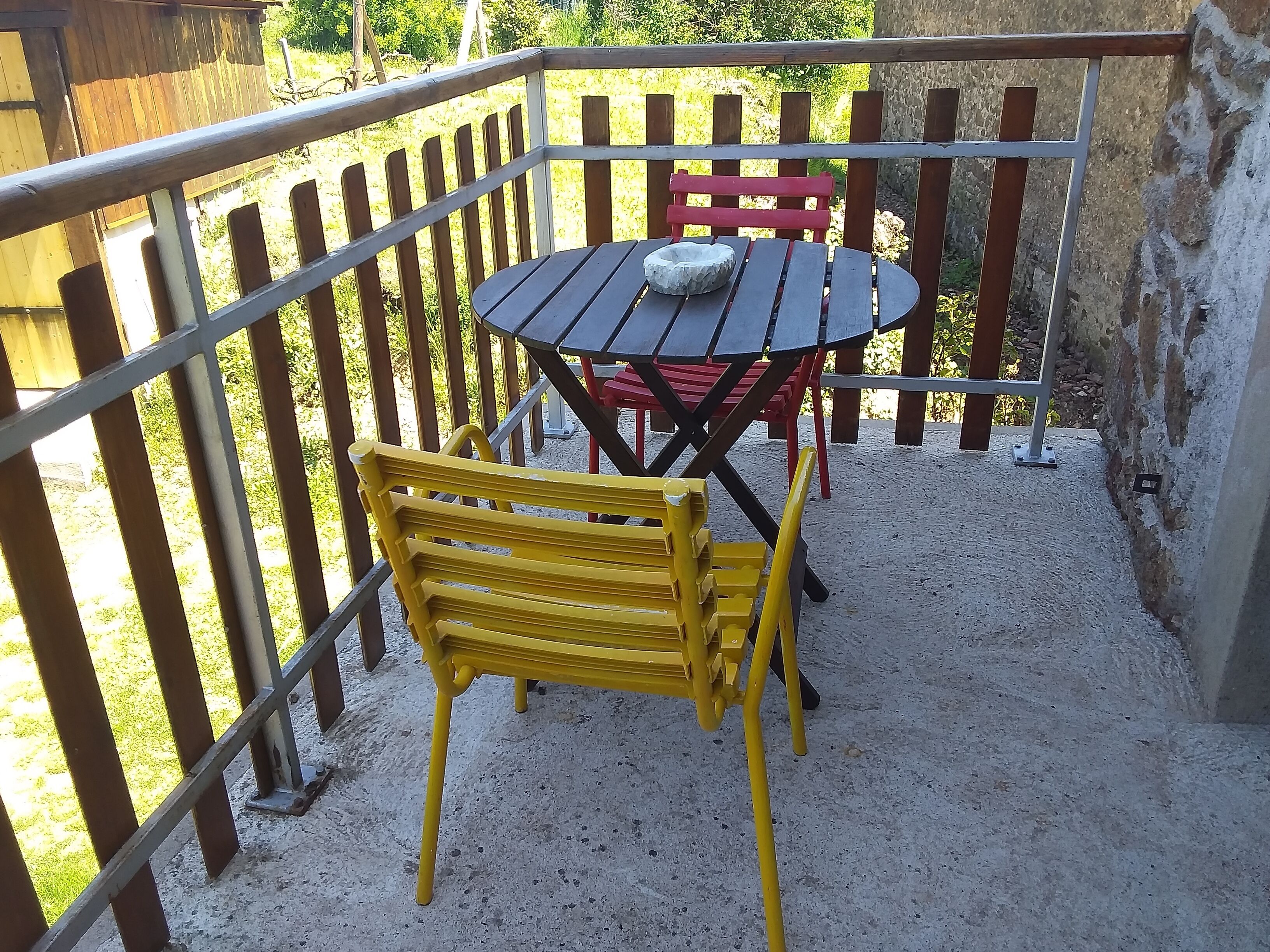 Une terrasse avec une table ronde et deux chaises, une chaise jaune et un banc rouge.