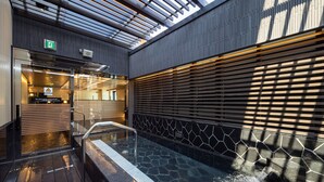 A modern indoor pool area with a wooden deck, a stone wall, and a skylight. - APA Hotel Ueno Ekimae (Tokyo)