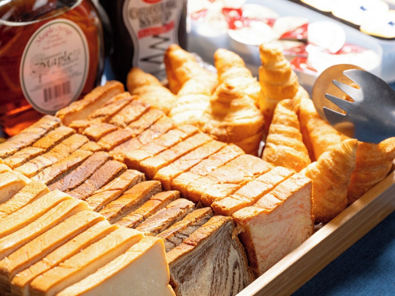 En bakke med forskellige kager og brød, heriblandt croissanter og en brødløb, med en gaffel ved siden af.