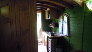 A rustic kitchen with wooden cabinets, a sink, and a window overlooking a green outdoor area. - Roulotte Gite Tsigane A 15km DES Sables D'olonne (Grosbreuil)
