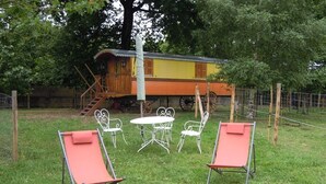 A wooden house with a balcony, surrounded by a fenced yard with two red lounge chairs and a metal table and chairs. - Roulotte Gite Tsigane A 15km DES Sables D'olonne (Grosbreuil)