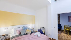 Ett modernt hotellrum med en säng, sängbord, ett skrivbord och en matplats med stolar.