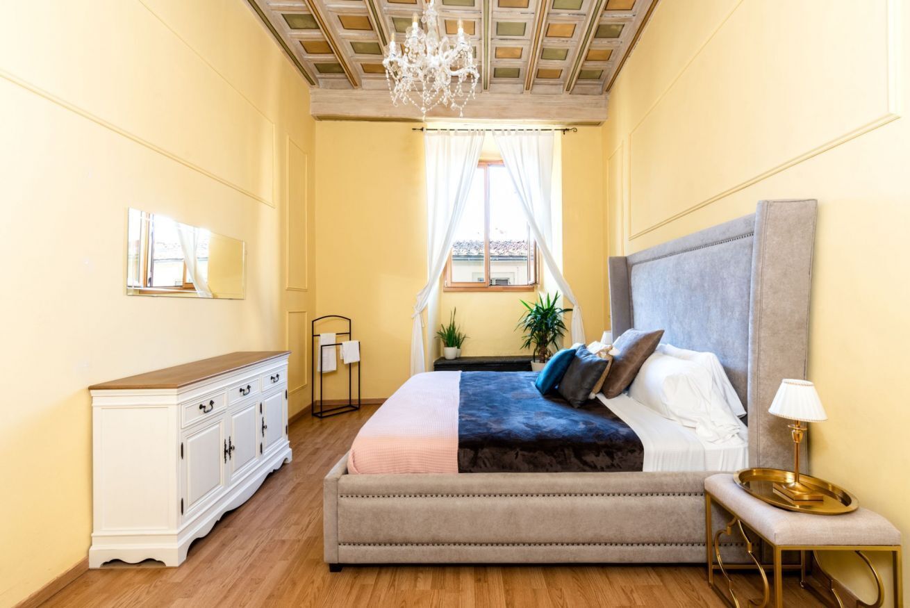 A bedroom with a bed, bedside table, lamp, and a mirror on the wall.