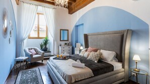 Ein Schlafzimmer mit einem großen Bett, einem Sessel, einem Nachttisch und einer Chandelier.