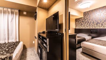 A compact hotel room with a bed, a desk with a television, a refrigerator, and a small seating area.