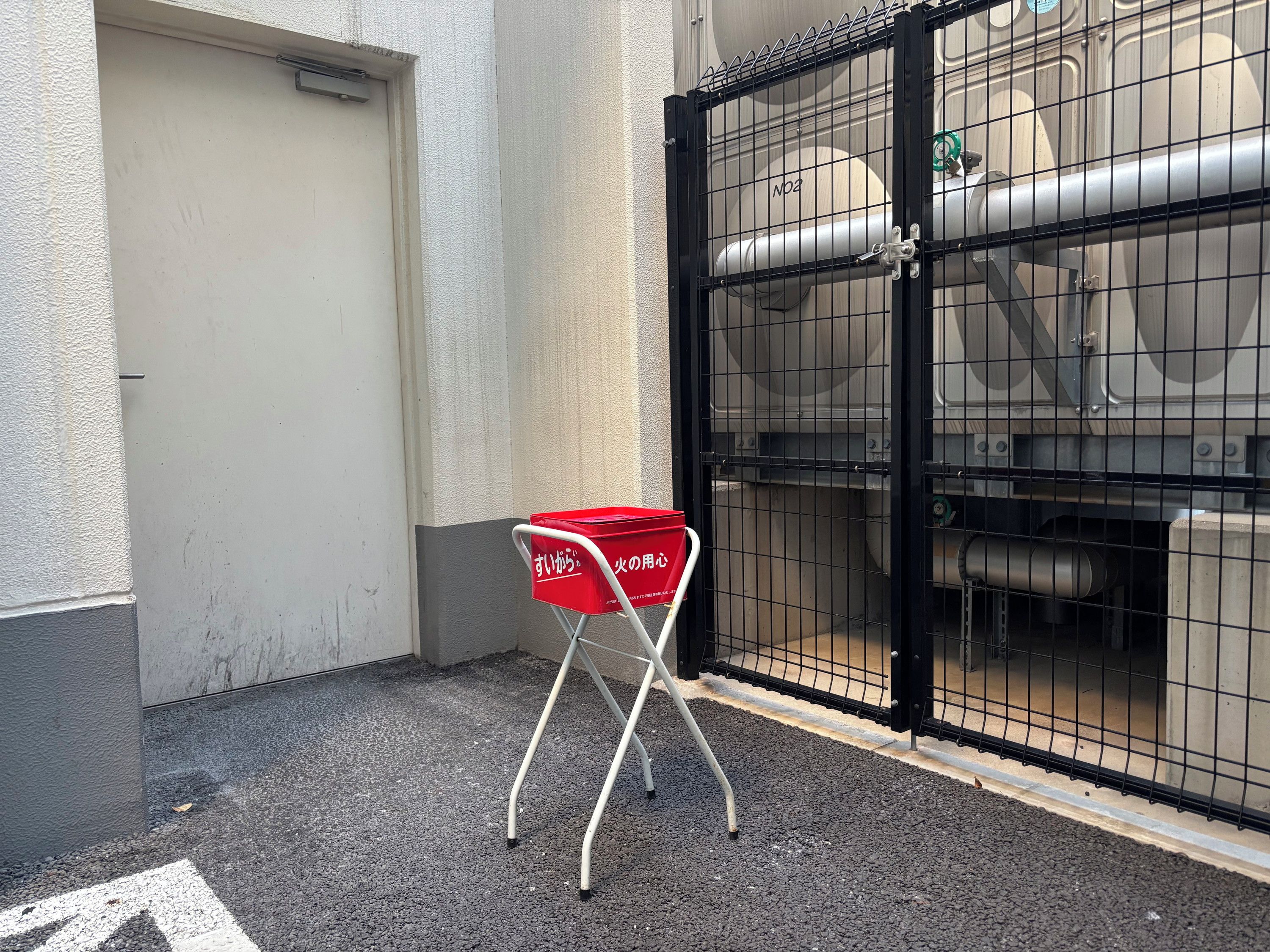 A red shopping basket on a metal stand next to a gated area with industrial equipment.