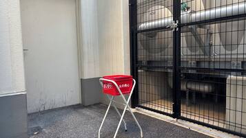 Una cesta roja de compras sobre un soporte metálico, cerca de un área vallada con maquinaria industrial.