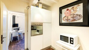 A compact kitchen with white cabinets, a microwave, and a small dining area with a white table and chair. - Historic center⭐ Minutes to attractions, Train and River (Firenze)