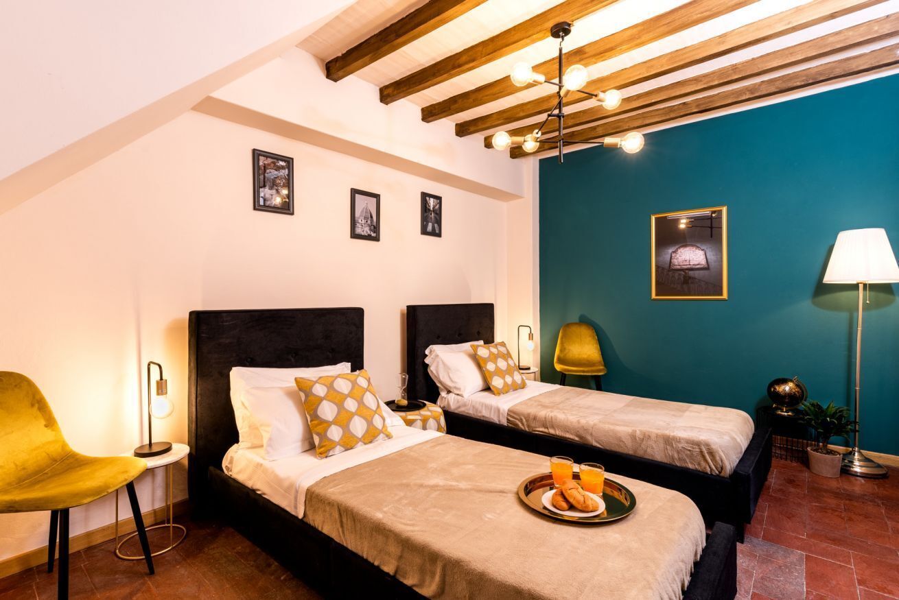 A hotel room with two beds, a yellow chair, a tray with breakfast, and a teal accent wall.