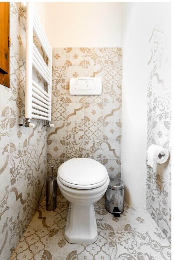 Une salle de bain avec des carreaux décorés, des toilettes, une poubelle et un porte-serviettes.